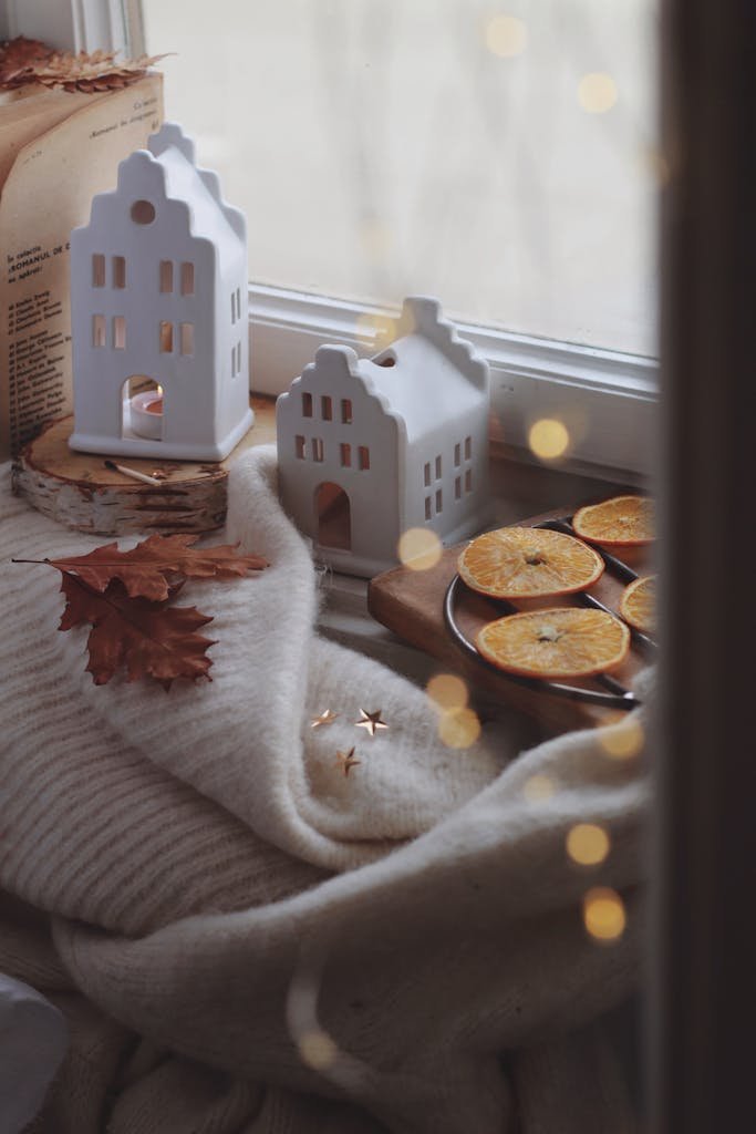 A cozy winter display by the window with mini houses, orange slices, and a soft sweater.