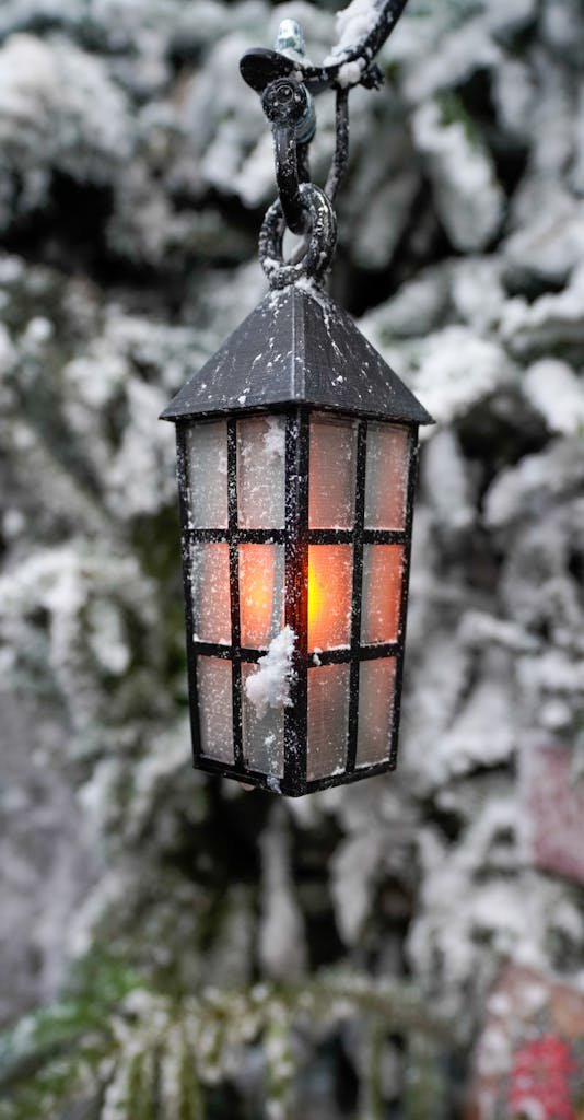 A glowing vintage lantern covered in snow against a winter backdrop, creating a cozy ambiance.