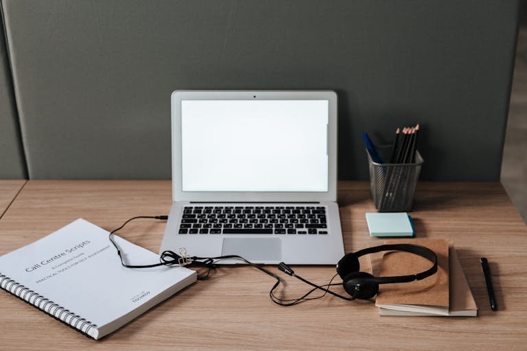 Minimalist workspace with laptop, headset, and call center scripts on a wooden desk.