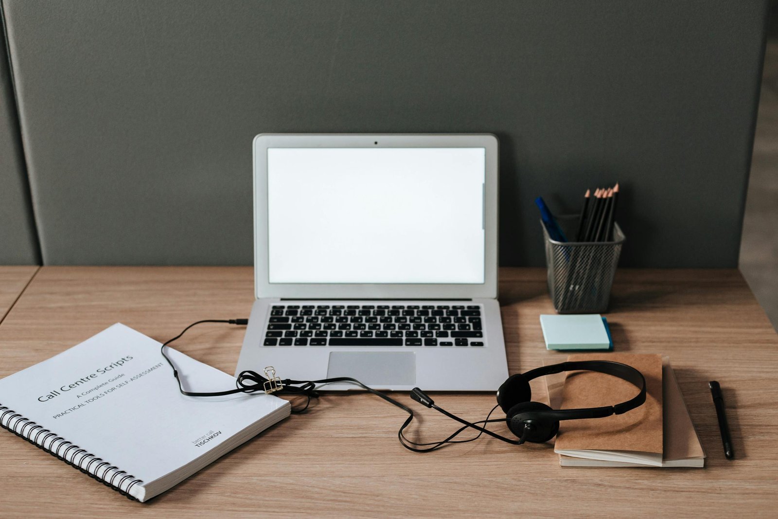 Minimalist workspace with laptop, headset, and call center scripts on a wooden desk.