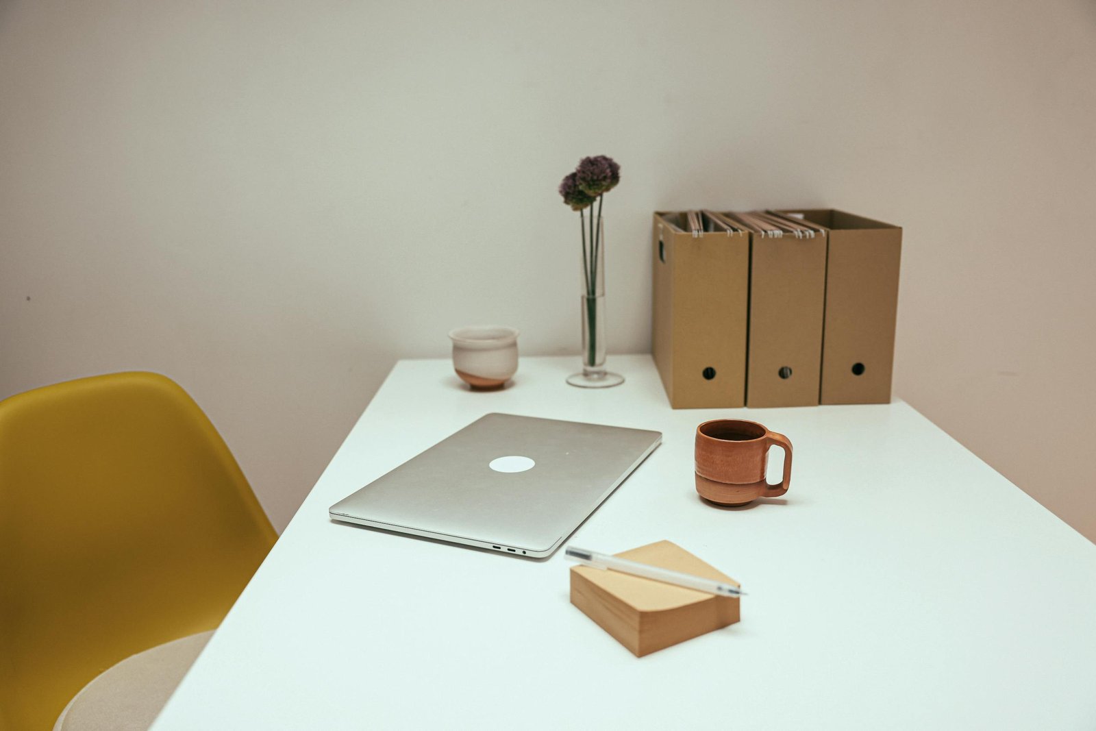 A minimalist workspace featuring a laptop, coffee cup, files, and a simple decor setup in an indoor office.
