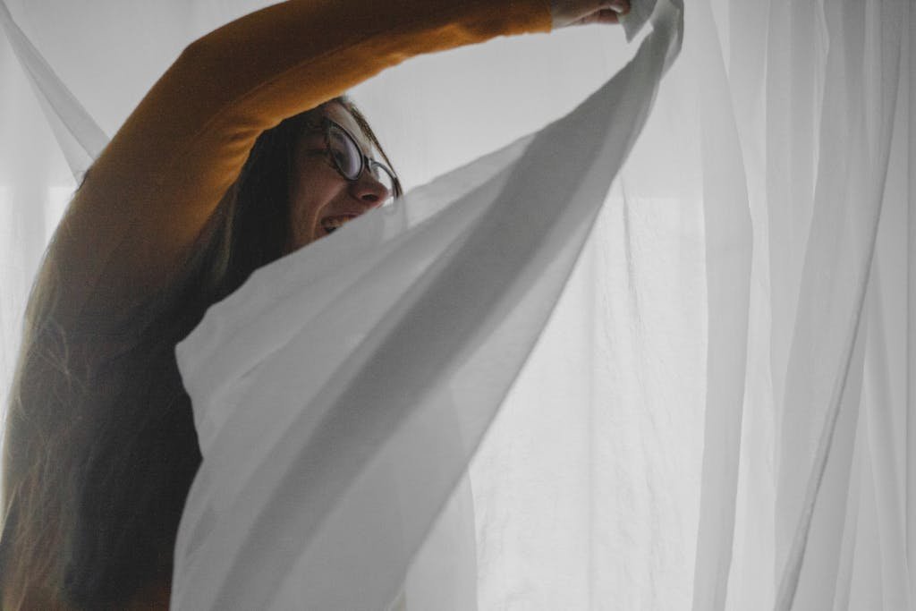 A cheerful woman enjoys a sunny day inside, playfully engaging with sheer curtains.