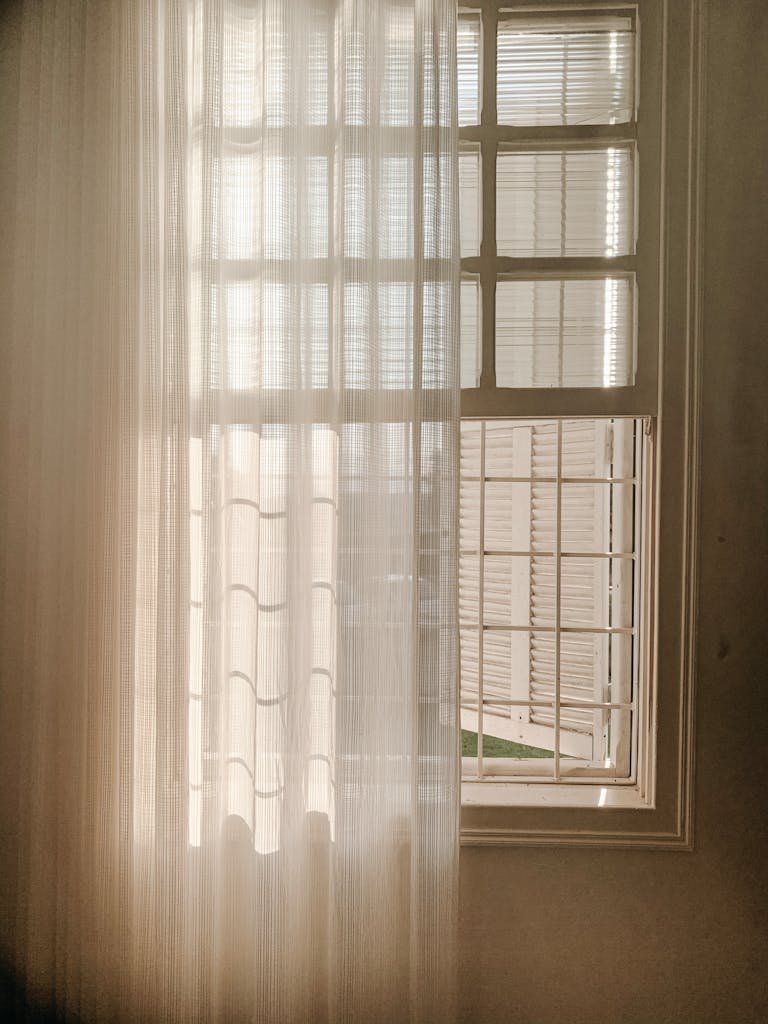 A serene view of sunlight filtering through sheer window curtains, casting soft shadows indoors.