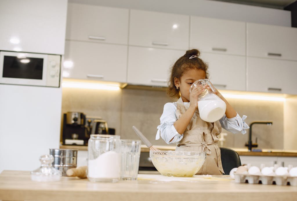 A young girl pours milk while baking in a contemporary kitchen environment.