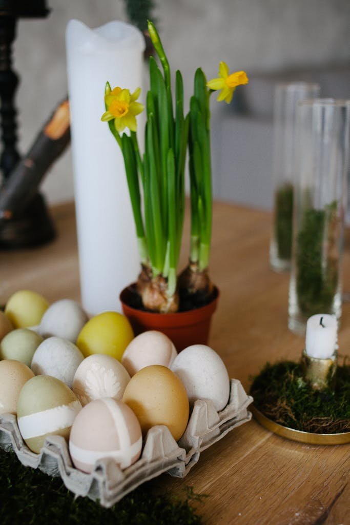 Decorative Easter setup with colorful eggs, daffodils, and candles on a wooden table.