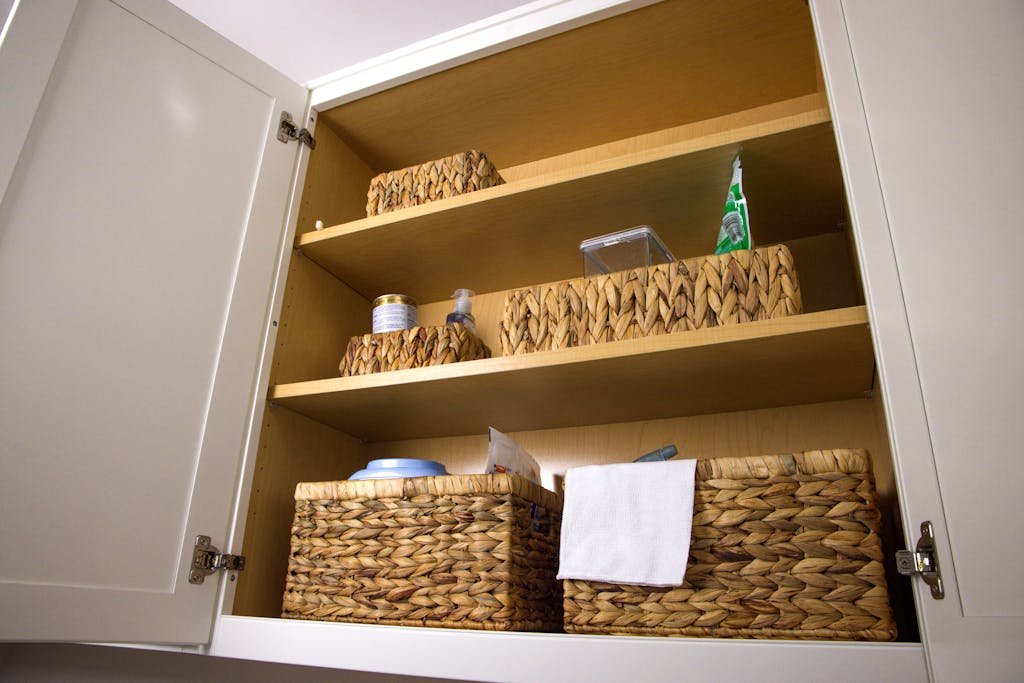 Neat storage in a kitchen cabinet using wicker baskets for a clean aesthetic and organization.