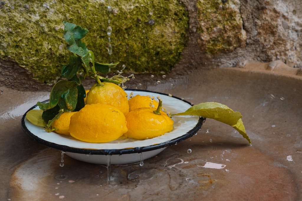 Vibrant yellow lemons in an enamel bowl with water droplets, against a rustic background.